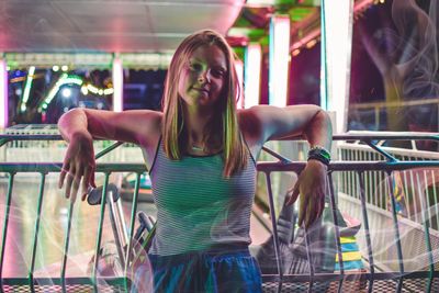 Portrait of smiling young woman standing by railing at night