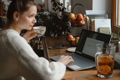 Young freelancer working on laptop at home. woman using computer on the kitchen for work. distant