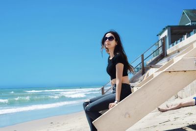 Portrait of young woman standing on beach against clear blue sky