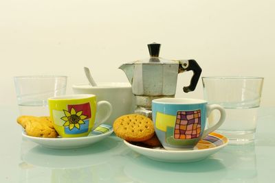 Close-up of espresso maker with cups and cookies on table