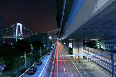 Light trails on road with illuminated rainbow bridge in background at night