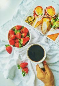 High angle view of woman holding coffee cup by strawberries at bedsheet