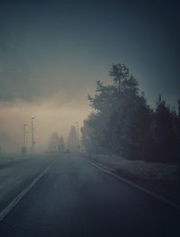 Empty road by trees against sky during foggy weather