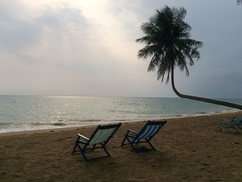 Empty chairs on beach against sky