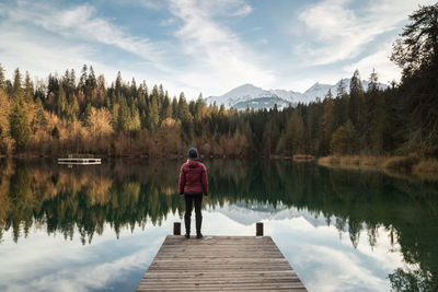 Rear view of human standing on pier over alpine lake against sky