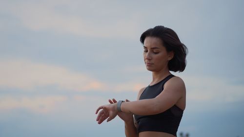 Side view of young woman exercising against sky during sunset