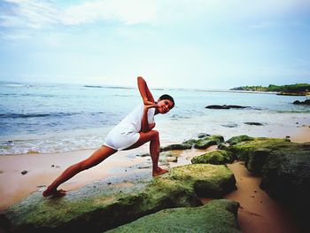 Young woman practicing yoga at beach against sky