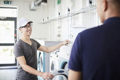 Smiling man talking to university friend while doing laundry