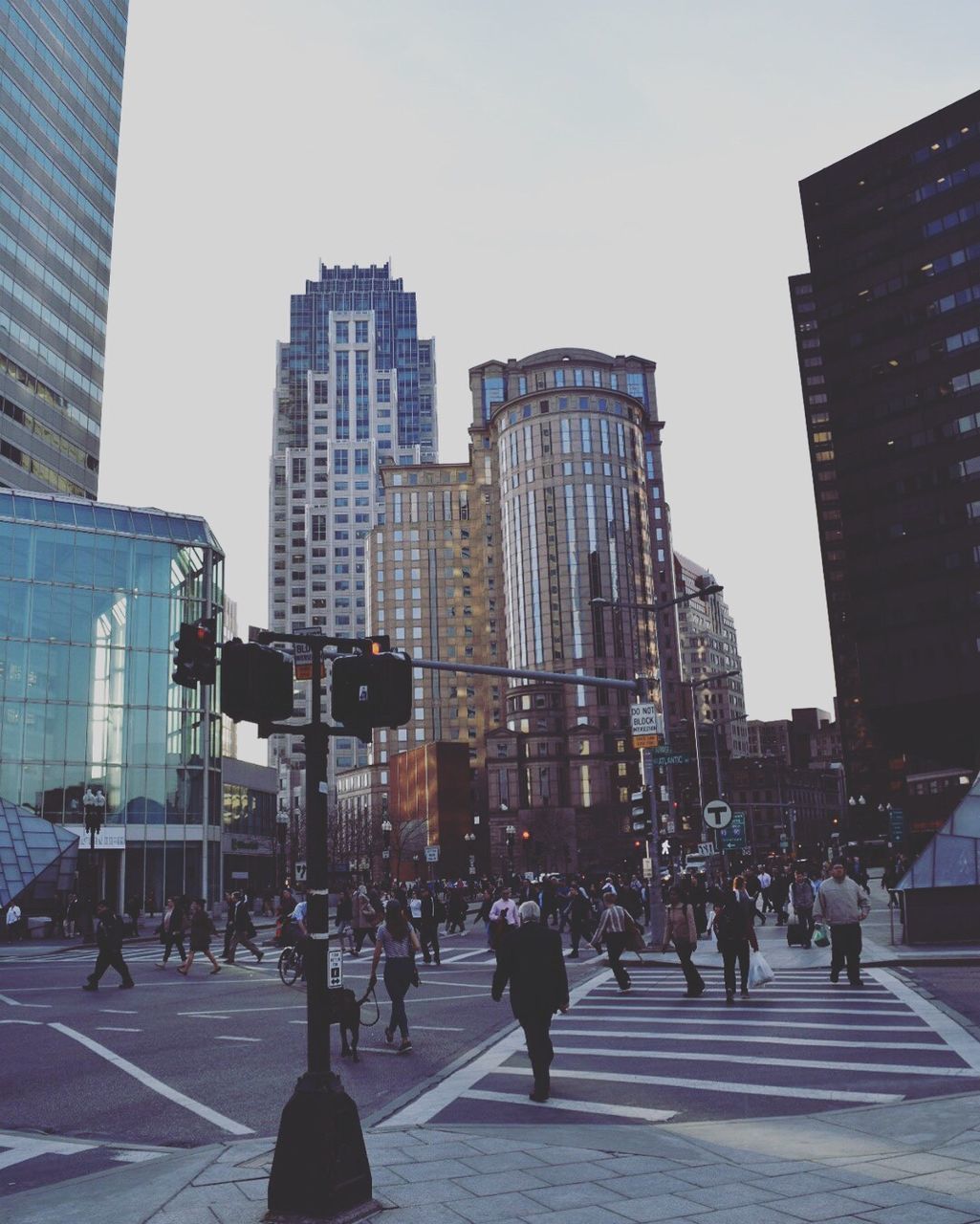 Crowd walking on city street by modern buildings against sky during sunset