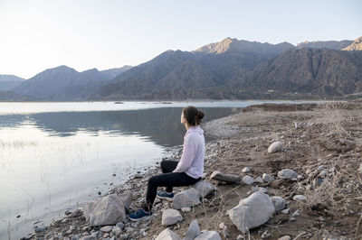 Woman meditating on the shore of a lake while enjoying the nature landscape.