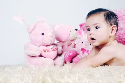 Cute baby girl lying by teddy bears on bed against white wall