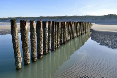 Wooden posts in river against sky