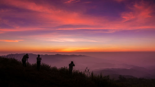 Panoramic view of silhouette people photographing mountains against sky during sunset