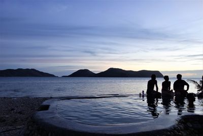 Silhouette people sitting on sea against sky during sunset