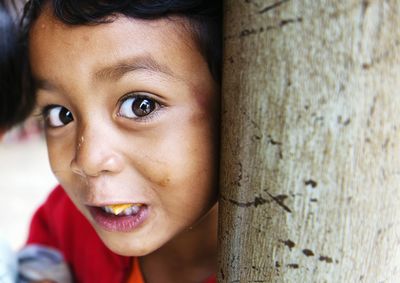 Close-up portrait of boy by tree trunk