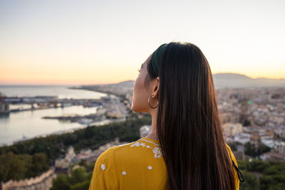 Portrait of young woman standing by cityscape against sky during sunset