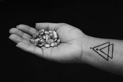 Cropped image of tattooed hand holding corn kernel against black background