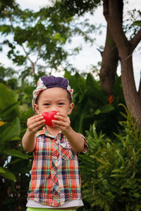 Portrait of cute boy holding heart shape against trees