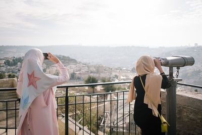 Rear view of man and woman standing on railing against sky