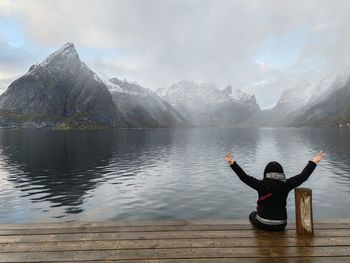 Rear view of woman doing yoga on lake against sky