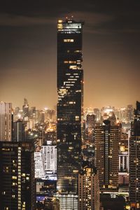 Illuminated modern buildings in city against sky at night