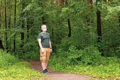 European young blond man in a disposable medical mask walks in the forest.