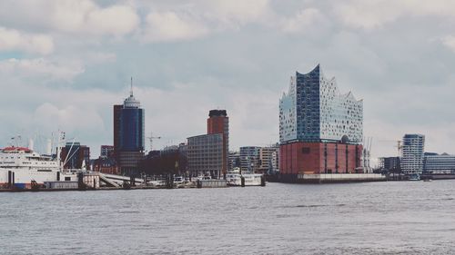 View of skyscrapers in river against cloudy sky