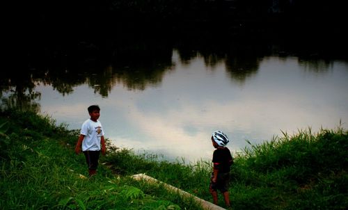 Rear view of boys standing on field by lake