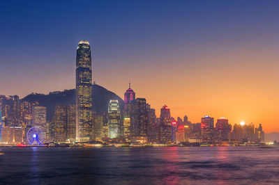 Illuminated buildings at waterfront during sunset