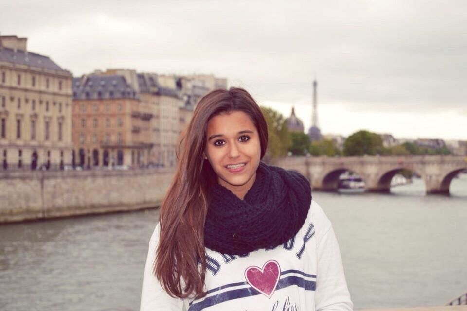 portrait, water, architecture, young adult, young women, looking at camera, bridge - man made structure, built structure, leisure activity, connection, focus on foreground, river, waterfront, front view, lifestyles, building exterior, long hair, smiling, waist up, person, city life, casual clothing, city, day, sky, medium-length hair, atmospheric mood