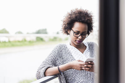 Woman standing on balcony looking at cell phone