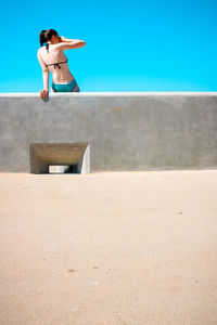 Woman sitting on retaining wall at beach against clear sky