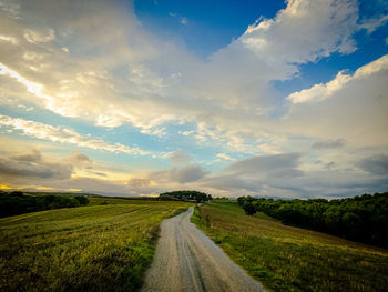 Road amidst field against sky during sunset