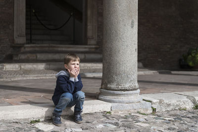 Boy sitting by column of old building