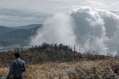 Rear view of man standing on land against sky.