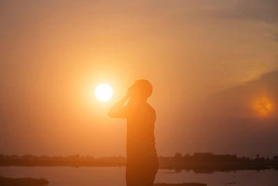 Silhouette woman standing against orange sky during sunset