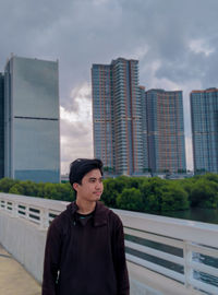 Portrait of young man standing against buildings in city