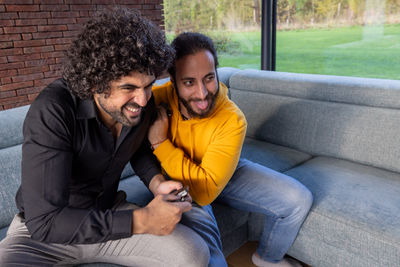 Side view of friends using mobile phone while sitting on sofa at home