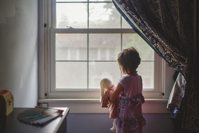 Rear view of girl looking through window at home