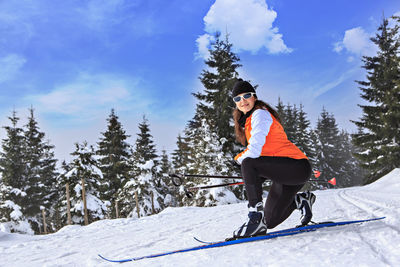 Portrait of woman wearing ski sitting on snow covered field 