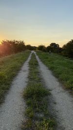 Empty road amidst field against sky during sunset