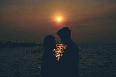 Side view of silhouette couple by sea against sky during sunset