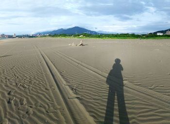 Shadow of man on sand at beach against sky