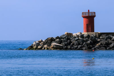 Lighthouse by sea against clear sky