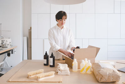 Female entrepreneur unpacking cardboard box containing bottles at table in workshop