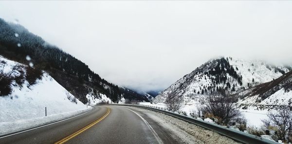 Road amidst snow covered mountains against clear sky