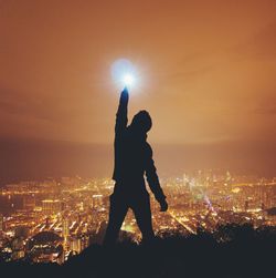 Silhouette of woman against illuminated cityscape during sunset