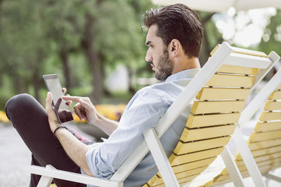 Young businessman using digital tablet on lounge chair at park