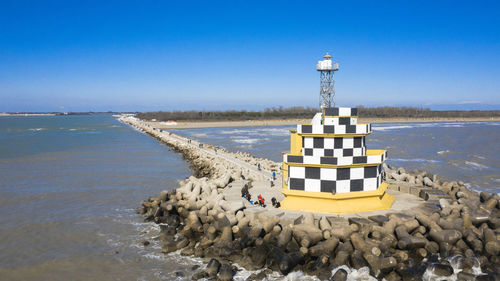 Lighthouse on beach against clear blue sky