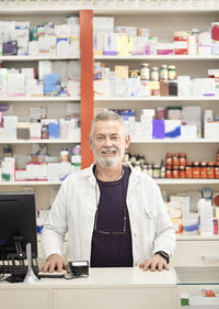 Smiling pharmacist standing at checkout counter in pharmacy store